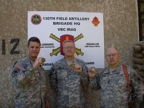 Service members holding challenge coins at the 130th Field Artillery Brigade Headquarters in Iraq